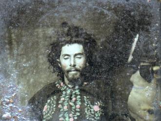 Death portrait of a bearded man holding a pistol across his chest