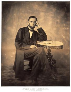 Sepia albumen portrait of Abraham Lincoln, seated with left arm on side table and head resting on hand.